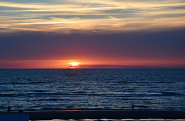 Sunset over the Ocean - View of the red sun sinking into the horizon and waves washing over the sand of the beach