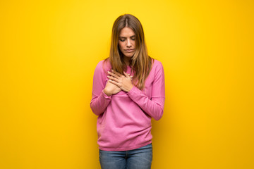Woman with pink sweater over yellow wall having a pain in the heart