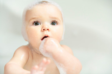 A Baby girl bathes in a bath with foam and soap bubbles