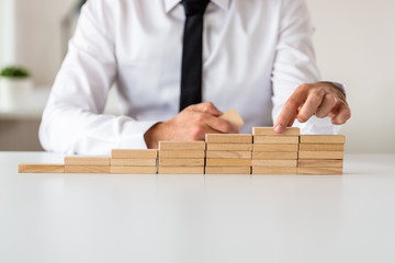 Businessman making stairs of wooden pegs in a conceptual image