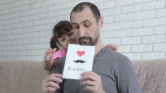 The child gives father a postcard. The little girl gave her dad a postcard. Father's day