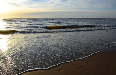 Sunset over the Ocean - View of the red sun sinking into the horizon and waves washing over the sand of the beach