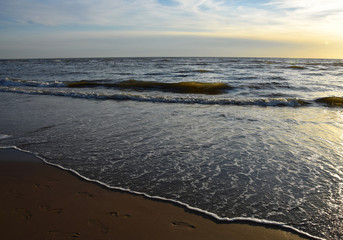 Sunset over the Ocean - View of the red sun sinking into the horizon and waves washing over the sand of the beach