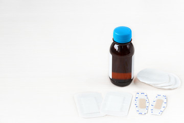 Close-up image of a bottle of alcohol, cotton wool and waterproof plasters  for the treatment of skin injuries on white wooden background 