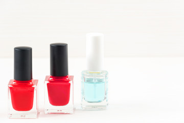 Close-up image of Two Red nail polish bottles and one colorless nail polish bottle on white wooden background.
