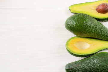 Close-up photo of avocados cut to half, brown seeds visible, with more avocados on white wooden background. Fresh sliced avocado.Vegetarian food concept.