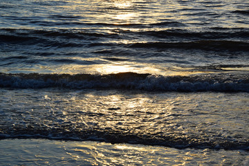 Sunset over the Ocean - View of the red sun sinking into the horizon and waves washing over the...