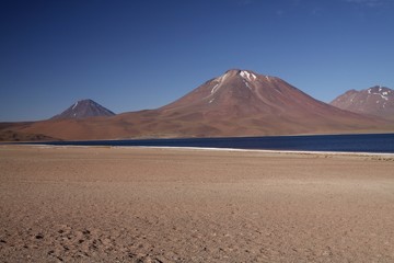 View on deep blue lake at Altiplanic Laguna (Lagoon) Miscanti in Atacama desert with partly snow capped cone of volcano Meniques in the background - Chile