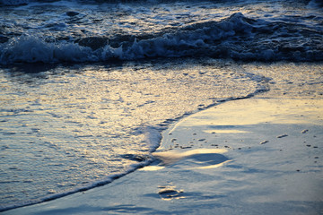 Sunset over the Ocean - View of the red sun sinking into the horizon and waves washing over the sand of the beach