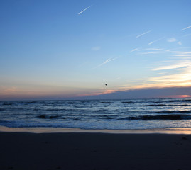 Sunset over the Ocean - View of the red sun sinking into the horizon and waves washing over the...