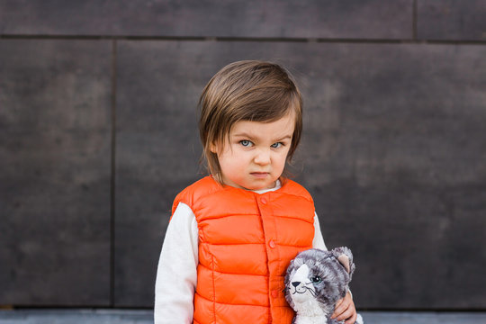 Emotional Funny Angry Child Girl Outdoor Portrait. Stubborn Baby With Her Toy Cat