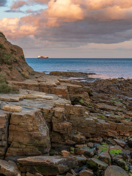 Evening Clouds and cliffs on the North Sea Coast in Cullercoats Bay, Tyne And Wear, England, UK - with a ship parking in the background