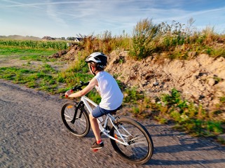 Little child boy in white helmet riding his bicycle
