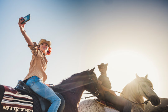Happy couple on vacation take picture selfie with smart phone during a ride with horses in outdoor leisure activity together - clear sky and sunset light for free people