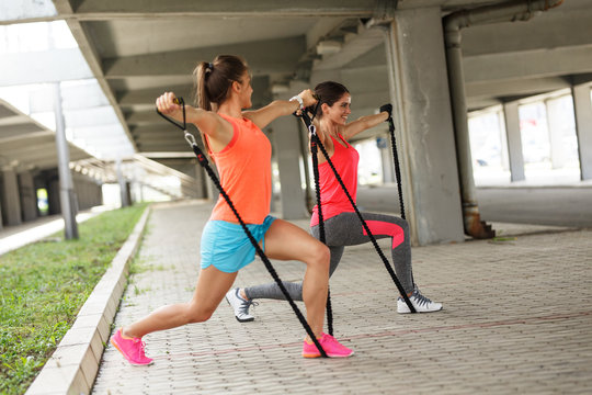 Two young female work out on trx,suspension trainer.Outdoor workout.