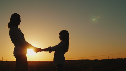 Mom holds her daughter's hands, stand alone at sunset. Single parent concept