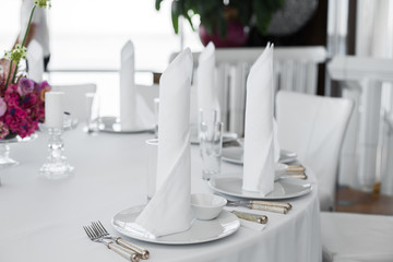 closeup white napkins stand in  white plates on served table in the restaurant. clean white dishes layout on a white tablecloth