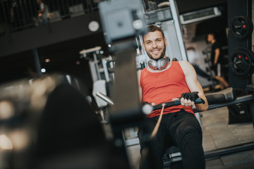 Young man doing workouts on a back with power exercise machine in a gym club
