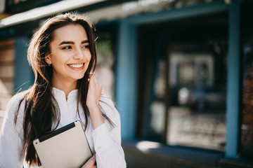 Beautiful caucasian businesswoman looking away and laughing while holding a tablet and touching her...
