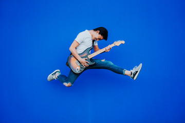 Naklejka na ściany i meble young man jumping with electric guitar on blue background
