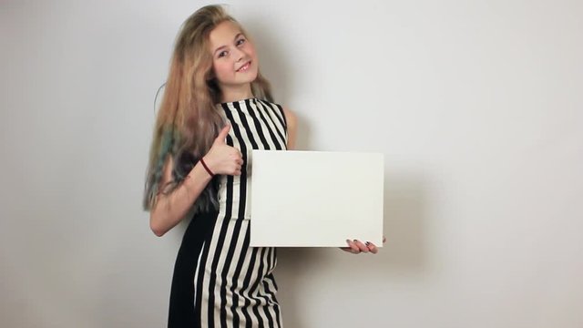 Beautiful teenage girl showing thumbs up gesture and holding in her hands blank canvas. Grey wall on background.
