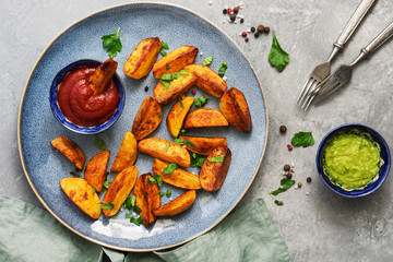 Fried potatoes with tomato sauce,guacamole, spices and greens in a plate on a gray background. Top view.