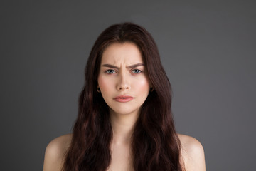 Close up portrait of beautiful girl with brunette hair frowning her face in displeasure with bare shoulders