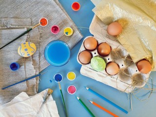 Eggs, colorful paints, brushes, pencils on a blue background, coloring eggs, preparing for Easter