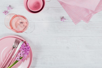 Pink rustic table setting with purple hyacinth flowers, linen napkin and glass of rose wine on white wooden table