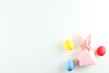 Pink Easter present box in a form of bag with bunny ears in minimal top view composition with colored chicken eggs, bright paper background. A lot of copy space for text. Close up, flat lay.