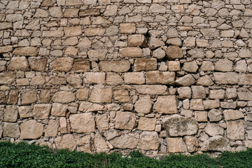 Old stone wall texture with green grass, blocks of ancient castle surface as background for design