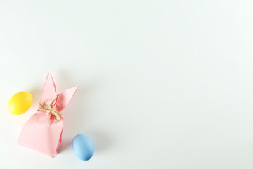 Pink Easter present box in a form of bag with bunny ears in minimal top view composition with colored chicken eggs, bright paper background. A lot of copy space for text. Close up, flat lay.
