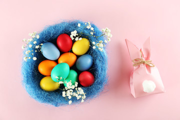 Different Easter eggs in straw nest, beautiful flat lay pastel colored composition on pale gradient paper background. Top view, copy space.