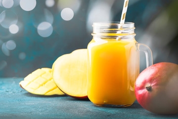 Freshly squeezed fresh mango juice in large glass jar with fresh fruit on dark blue tropical background, copy space, selective focus