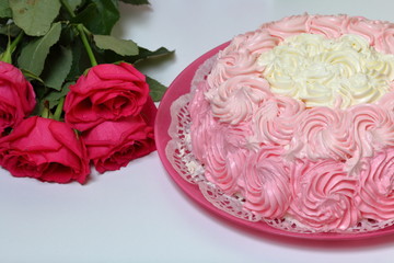 Biscuit cake, decorated with a cream with shades of pink. Nearby is a bouquet of roses. On a white background.