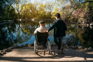 56 year old male sitting on a wheelchair and he young friend in the park