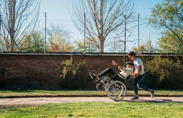 56 year old male sitting on a wheelchair and he young friend happy in the park