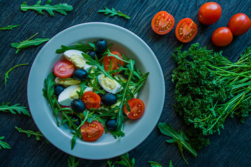 Greek salad with fresh tomatoes, arugula, eggs, olives with olive oil on a dark wood background. Healthy food. Veggie dish.