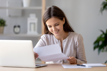 Happy satisfied woman sitting at desk reading positive letter