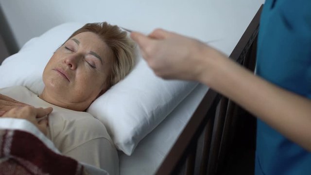 Sick-nurse covering sleeping elderly patient with blanket, taking family photo