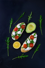 Sandwiches with tomato, mozzarella, arugula and curd cheese on a black table
