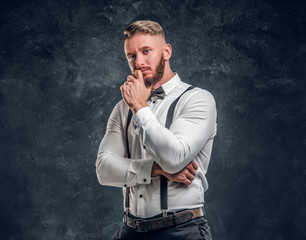 Pensive male thinking about something important. Stylishly dressed young man in shirt with bow tie and suspenders posing with hand on chin.