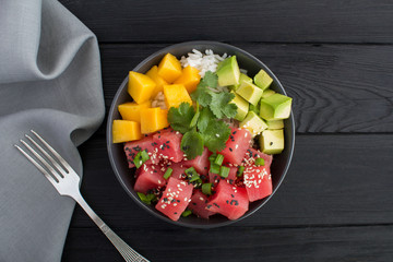 Poke salad in the dark bowl in the center of the black wooden background.Top view.Closeup.