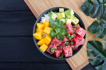 Poke salad in the dark bowl on the tropical background.Top view.Copy space.