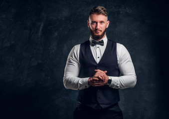 Elegantly dressed bearded hipster in a vest with bow tie. Studio photo against a dark wall background
