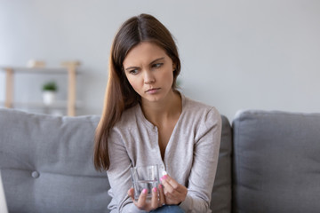 Frustrated pensive woman holding pill and glass of water