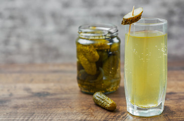 Pickle juice in glass and a can of pickled cucumbers on wooden table background