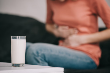 cropped view of woman with lactose intolerance holding stomach near glass of milk
