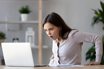 Shocked woman looking at laptop screen surprised with bad news