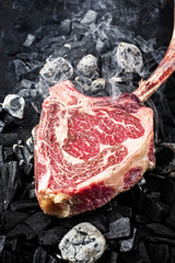 Traditional raw dry aged wagyu tomahawk steak on hot burning charcoal with smoke as closeup on a barbecue fire